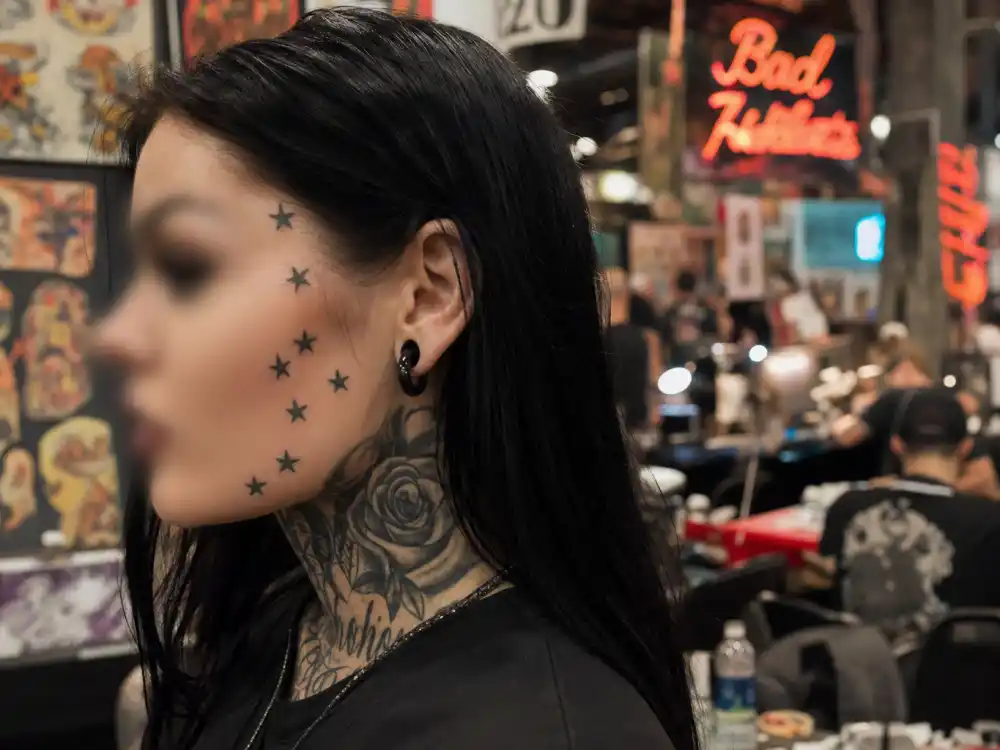 Kat Von D tattoos and their meanings — cluster of star tattoos near left temple and cheekbone in blurred side profile backstage