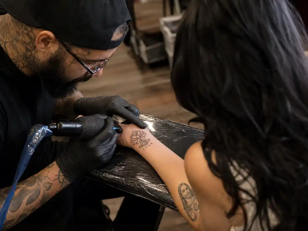 Katy Perry tattoos and their meanings — tattoo artist inking wrist lotus and eye Saturn tour tattoo during professional studio session