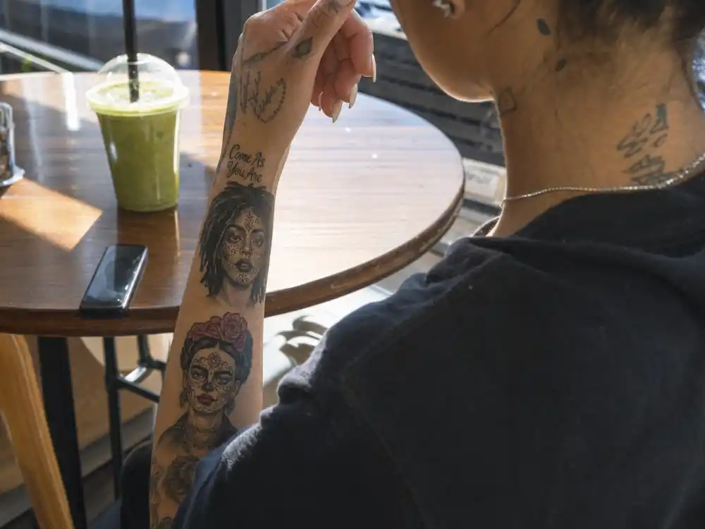Kehlani tattoos and their meanings — Lauryn Hill and Frida Kahlo portrait tattoos on upper arm in editorial over-shoulder angle