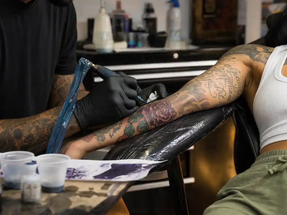 Kehlani tattoos and their meanings — tattoo artist inking forearm during professional studio session with existing sleeve work visible