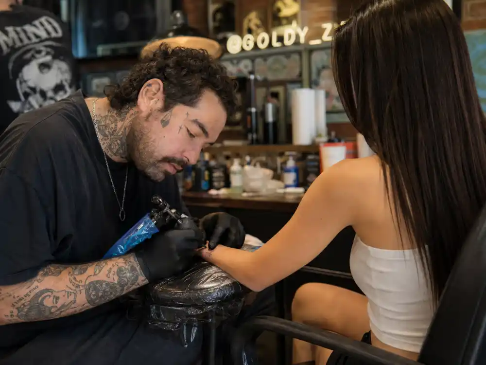 Kendall Jenner tattoos and their meanings JonBoy studio — celebrity tattoo artist gloved hands applying fine-line finger ink on brunette model from behind