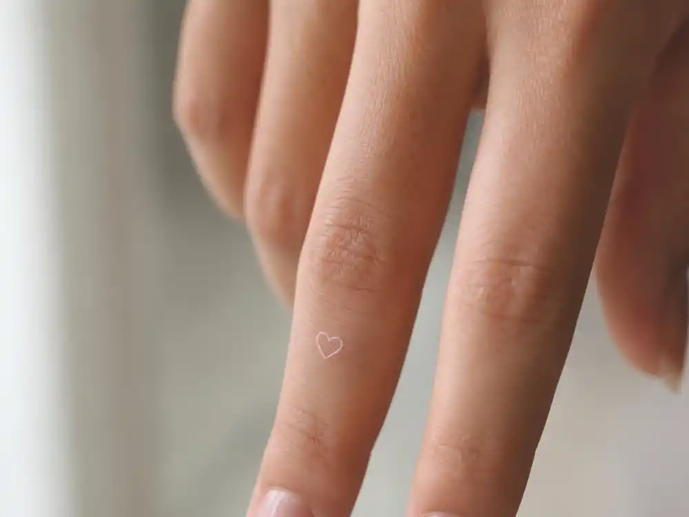 Kendall Jenner tattoos and their meanings white heart finger — tiny white ink heart tattoo on middle finger close-up from first JonBoy session
