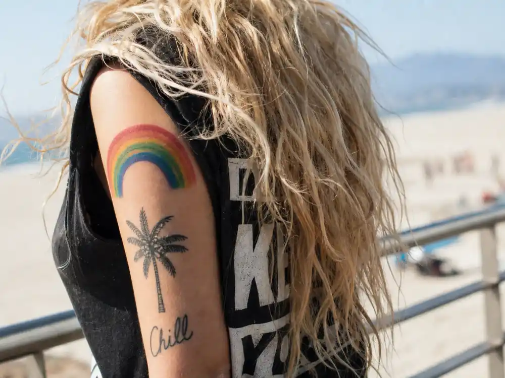 Kesha tattoos and their meanings — rainbow and palm tree chill tattoos on upper arm as luck charm ink
