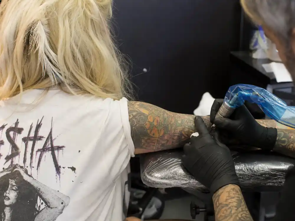 Kesha tattoos and their meanings — tattoo artist inking colorful forearm during professional studio session