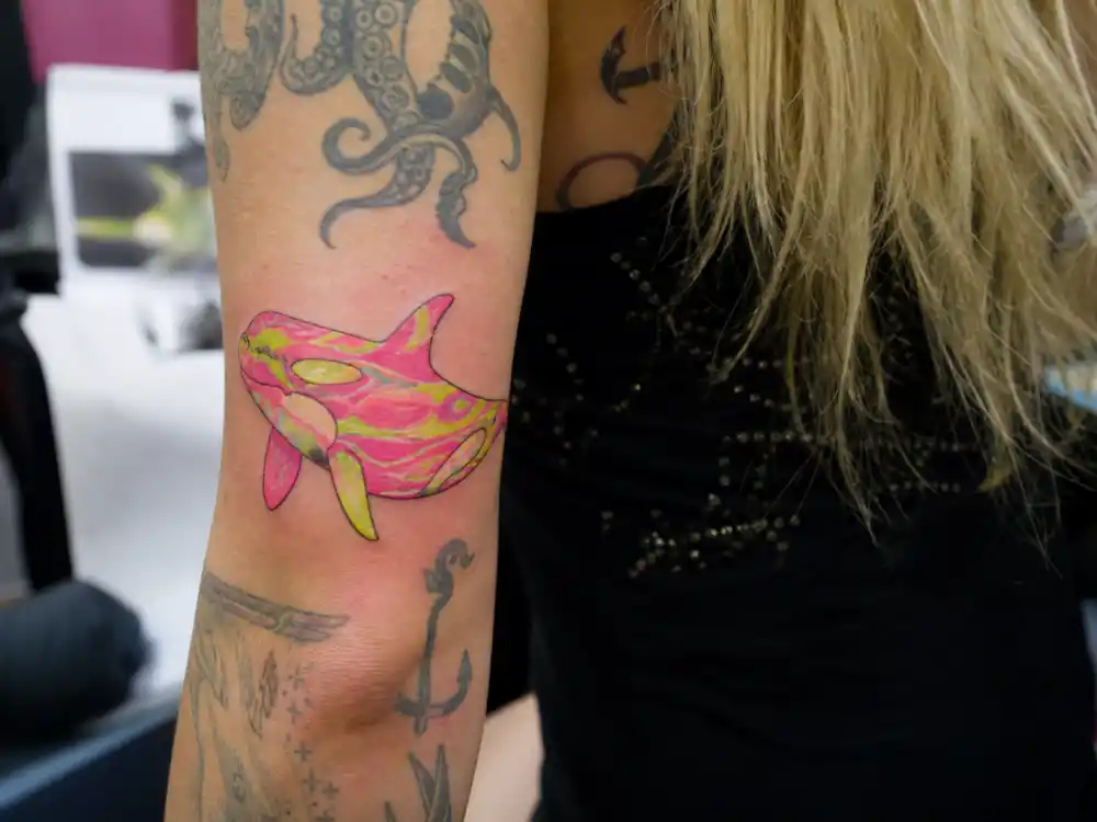 Kesha tattoos and their meanings — psychedelic neon orca whale tattoo on forearm from marine life collection