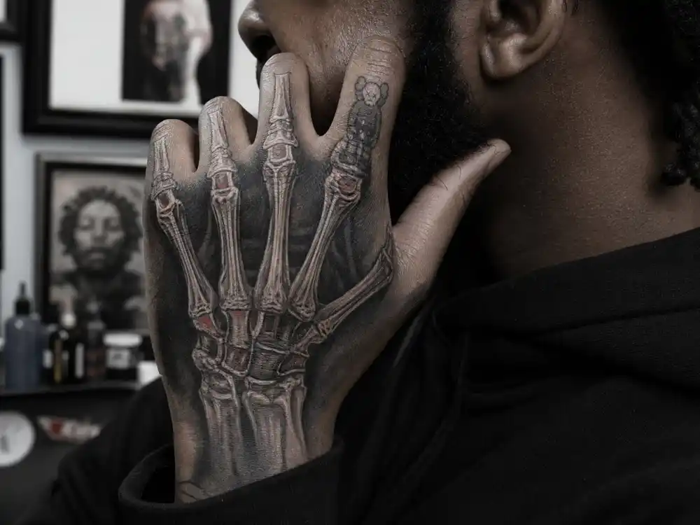 Kid Cudi tattoos and their meanings — anatomical skeleton hand tattoo covering fingers with companion figurine on index finger