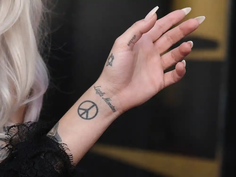 Lady Gaga tattoos and their meanings — close-up of peace sign wrist tattoo on left hand inspired by John Lennon