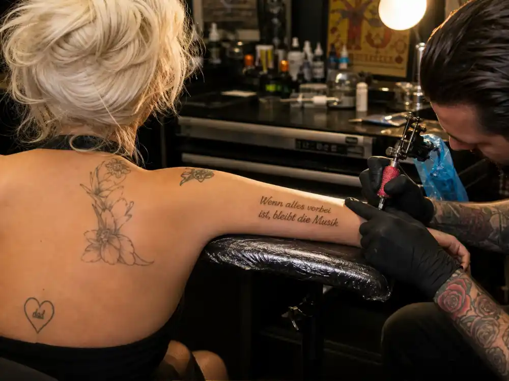 Lady Gaga tattoos and their meanings — tattoo artist inking German Rilke quote on inner arm during professional studio session