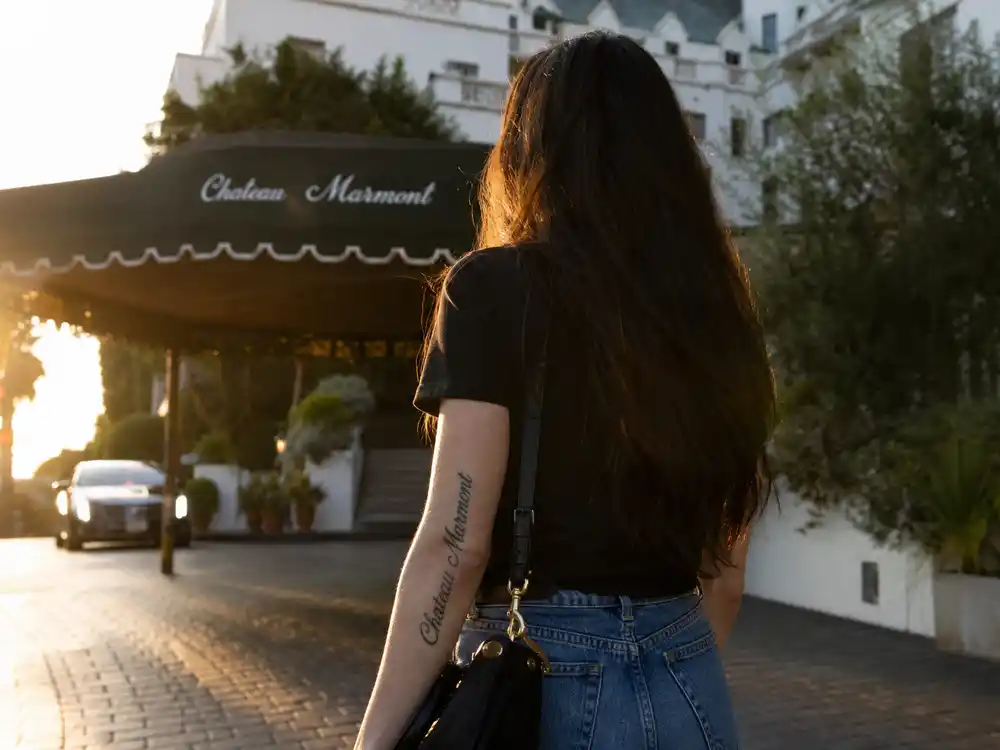 Lana Del Rey tattoos and their meanings Chateau Marmont — hotel name script tattoo on left forearm at Los Angeles boulevard golden hour