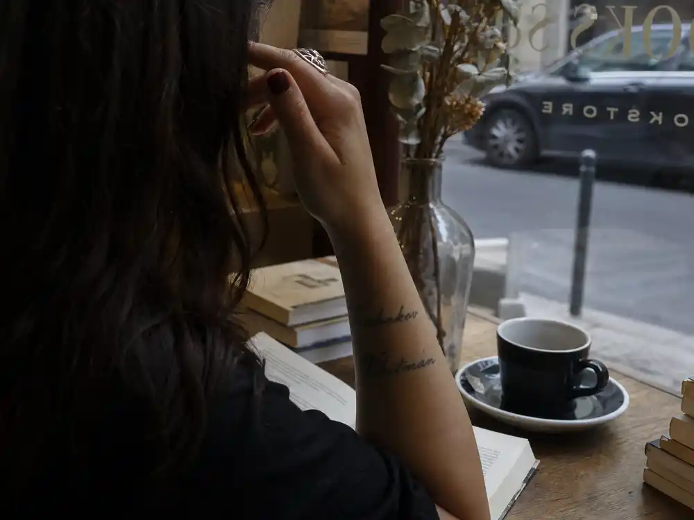 Lana Del Rey tattoos and their meanings Nabokov Whitman — writer name script tattoos on right forearm close-up at literary cafe