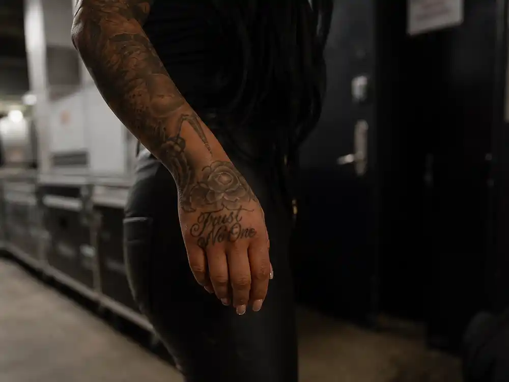Lana Del Rey tattoos and their meanings Trust No One — cursive script tattoo on right hand close-up at backstage hallway