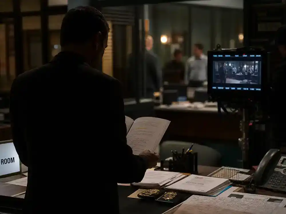 Law and Order SVU season 27 cast guide Benson squad — police captain silhouette from behind at squad room desk reviewing script on generic TV procedural film set