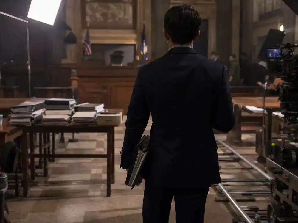 Law and Order SVU season 27 cast guide Carisi — ADA prosecutor silhouette from behind at courtroom film set with legal files and camera dolly track