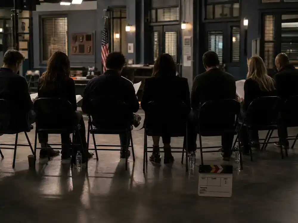 Law and Order SVU season 27 cast guide ensemble — TV drama cast silhouettes from behind rehearsing on police precinct interior film set with clapperboard