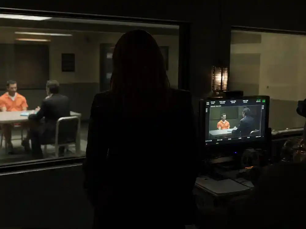 Law and Order SVU season 27 cast guide Rollins — detective actor silhouette from behind at interrogation room film set with two-way mirror and director monitor
