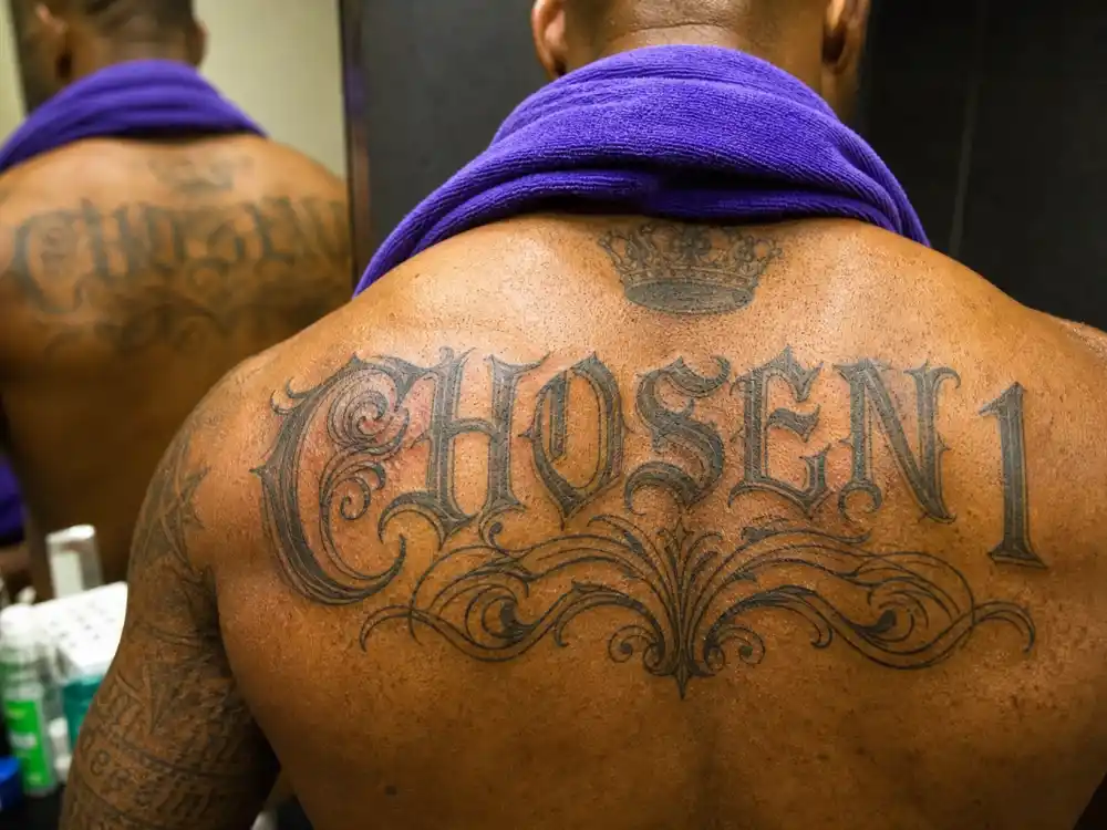 LeBron James tattoos and their meanings — close-up of CHOSEN 1 script tattoo across upper back in locker room mirror