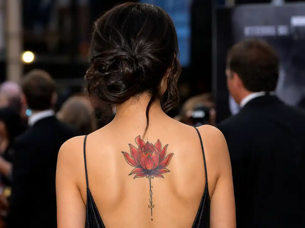 Lena Headey tattoos and their meanings lotus — colorful red lotus flower tattoo on upper back Buddhist purity compassion symbolism