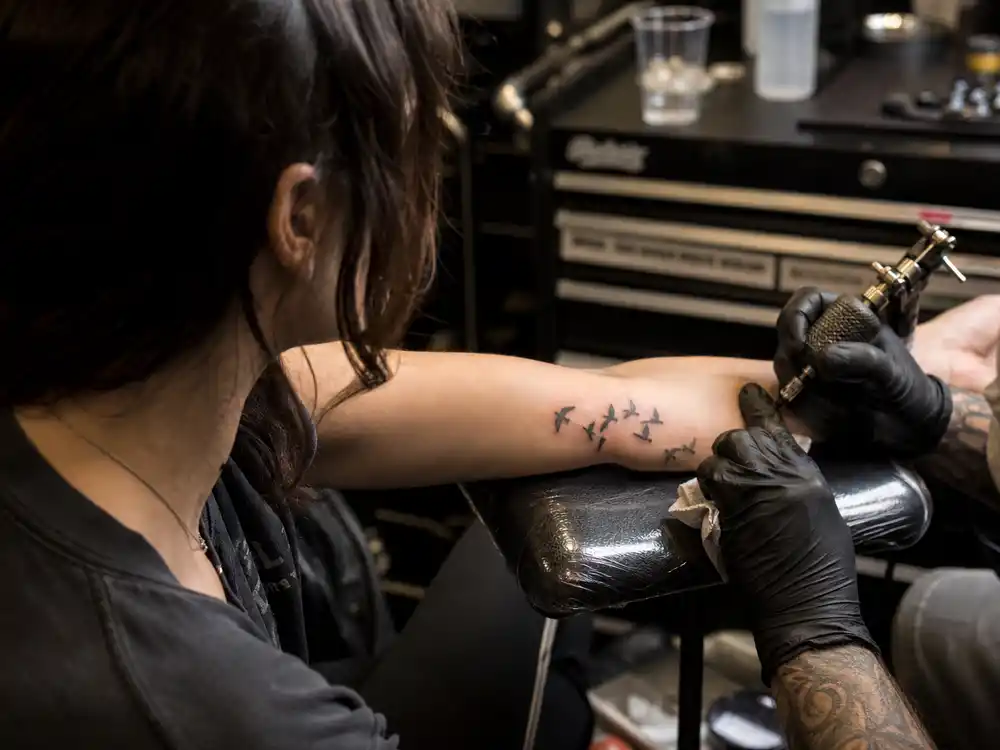 Lena Headey tattoos and their meanings studio — tattoo artist applying flock of birds ink on forearm during body art session