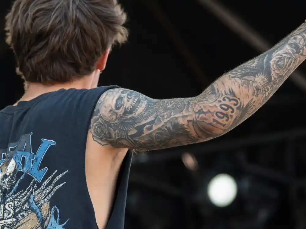 Liam Payne tattoos and their meanings arm sleeve — skull lion 1993 and rose eagle black-grey forearm tattoos over-shoulder stage angle