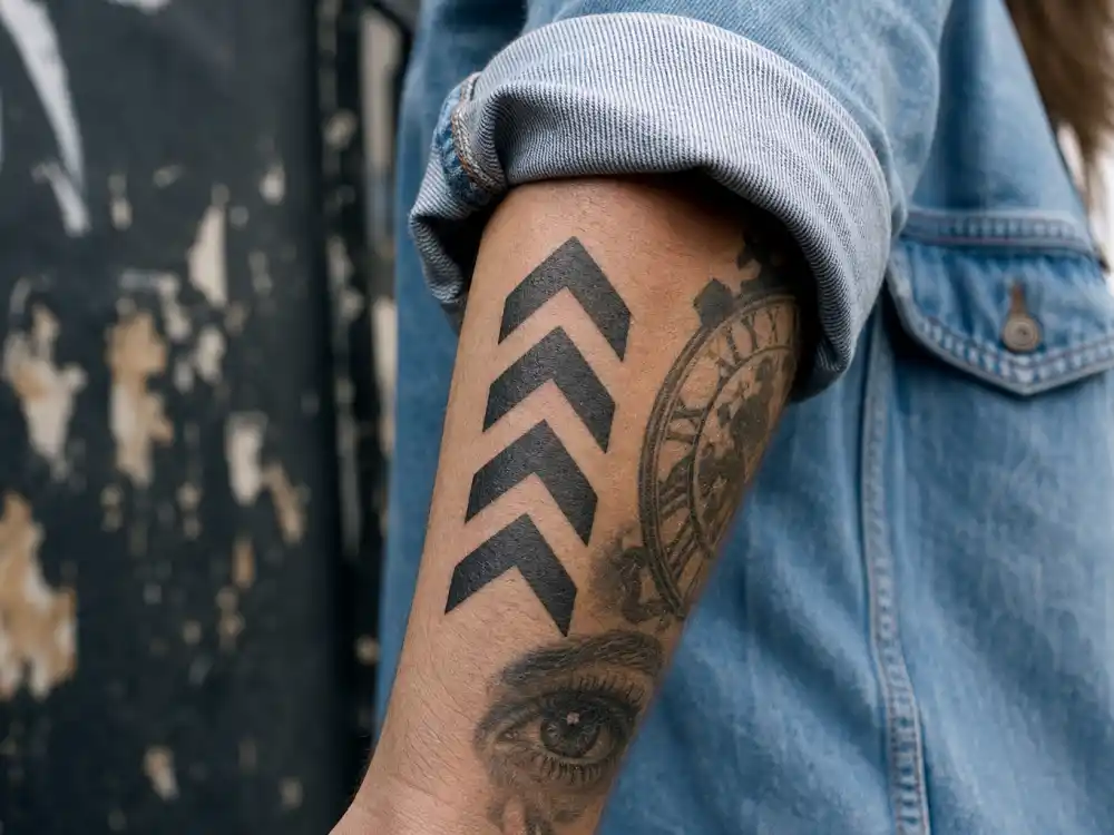 Liam Payne tattoos and their meanings chevron arrows — bold upward arrow forearm tattoo with clock and eye designs in black-grey ink