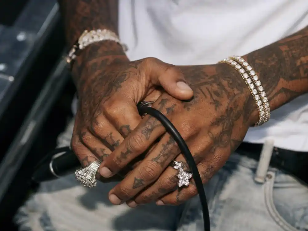 Lil Uzi Vert tattoos and their meanings — tattooed fingers and knuckles with letter ink on rapper hands holding microphone backstage