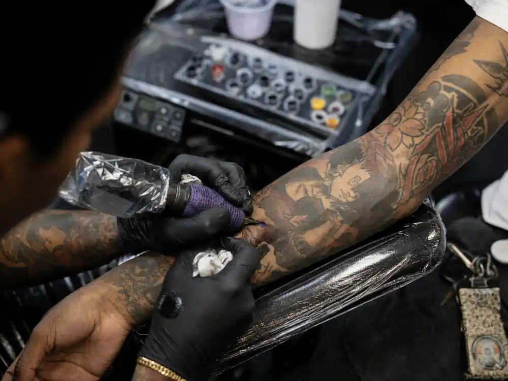 Lil Uzi Vert tattoos and their meanings — tattoo artist working on forearm sleeve in professional studio session with existing colorful ink
