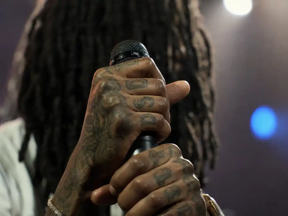 Lil Wayne tattoos and their meanings — tattooed fingers and knuckles with letter ink on rapper hands holding microphone backstage
