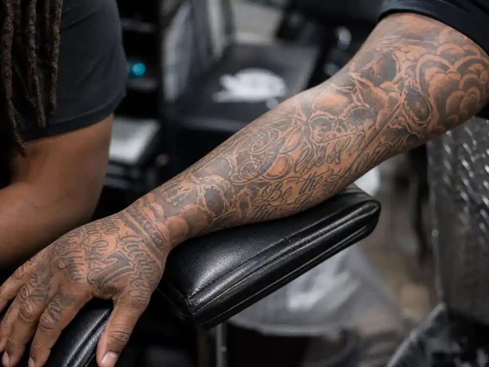 Lil Wayne tattoos and their meanings — close-up of heavily tattooed forearm sleeve with script and skull motifs on rapper arm