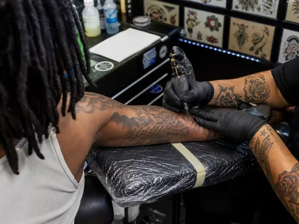 Lil Wayne tattoos and their meanings — tattoo artist working on forearm sleeve in professional studio session with existing dense ink