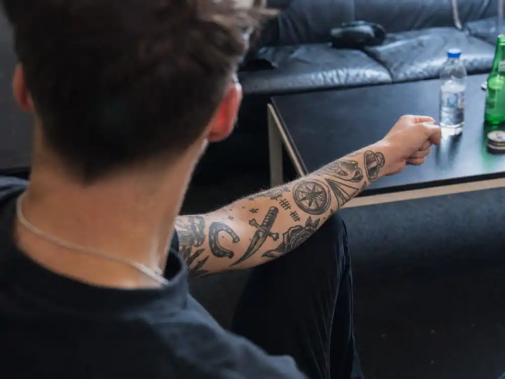 Louis Tomlinson tattoos and their meanings arm sleeve — patchwork dagger compass tea cup tally marks forearm tattoos over-shoulder angle