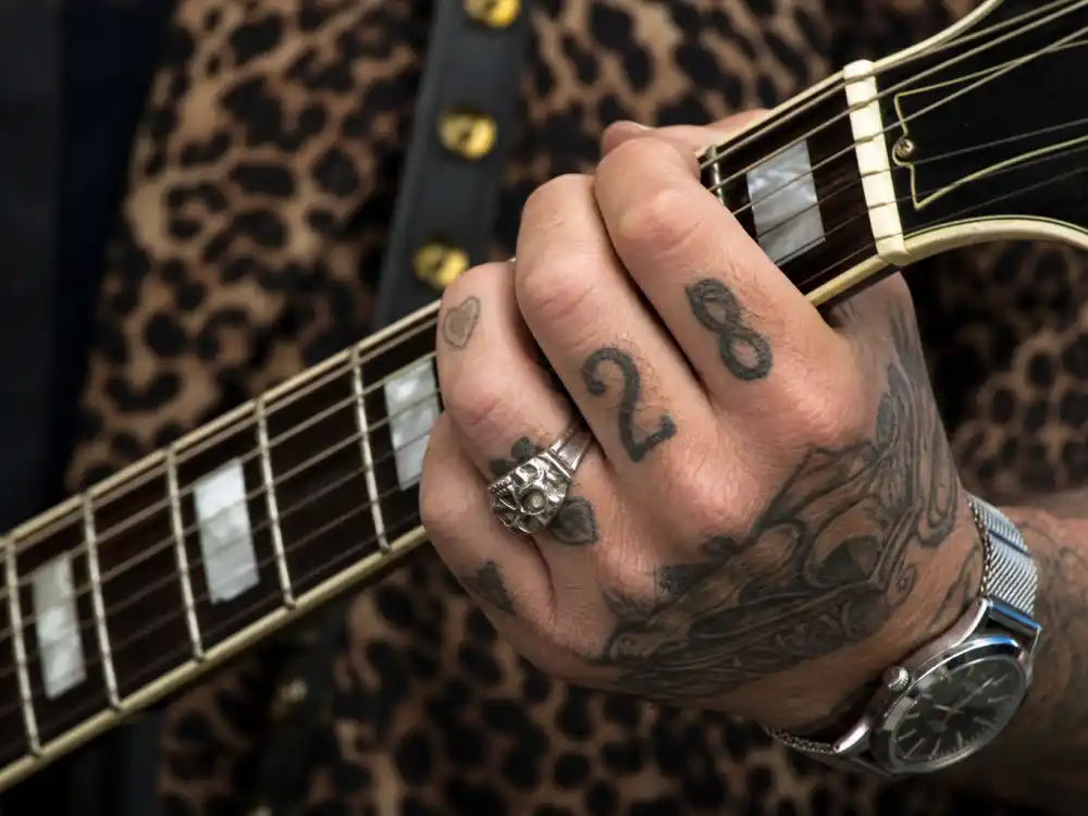 Louis Tomlinson tattoos and their meanings hand tattoos — number 28 finger ink and knuckle symbols close-up holding guitar neck