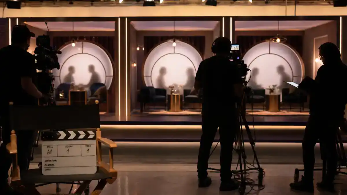 Love Is Blind season 8 cast guide — reality TV dating show pod soundstage with partitioned booths camera crew silhouettes and clapperboard on director chair