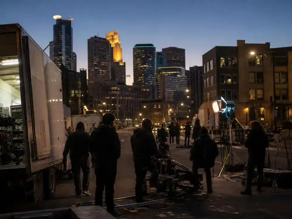 Love Is Blind season 8 cast guide Minneapolis — skyline at dusk with film production trucks and camera dolly on urban street for reality TV location shoot