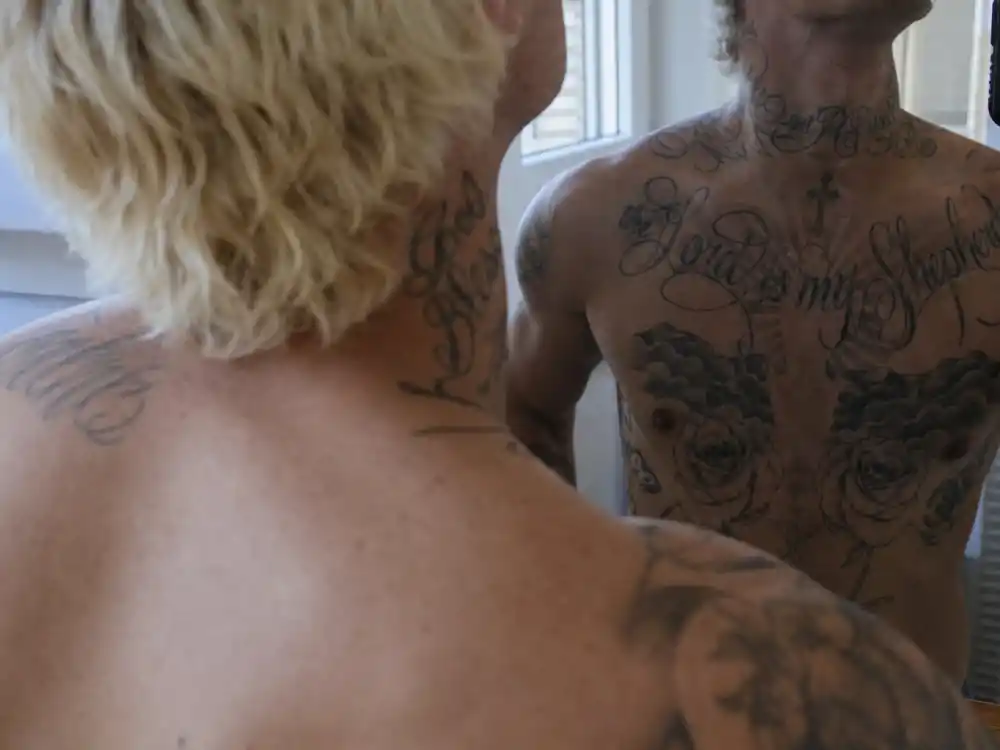 Machine Gun Kelly tattoos and their meanings chest piece — script and cross ink on collarbone and sternum mirror selfie angle