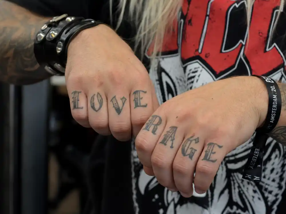 Machine Gun Kelly tattoos and their meanings hand ink — close-up of knuckle script tattoos on tattooed fingers and forearms