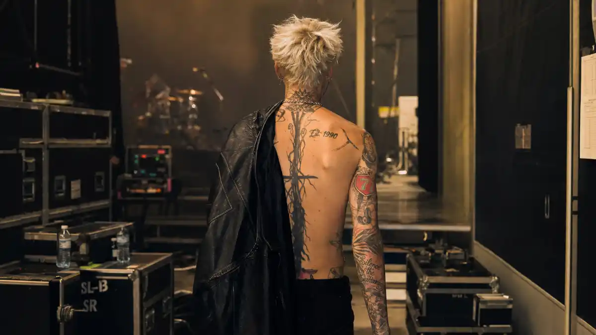 Machine Gun Kelly tattoos and their meanings — bleached blonde rock musician from behind showing arm sleeve and neck ink backstage