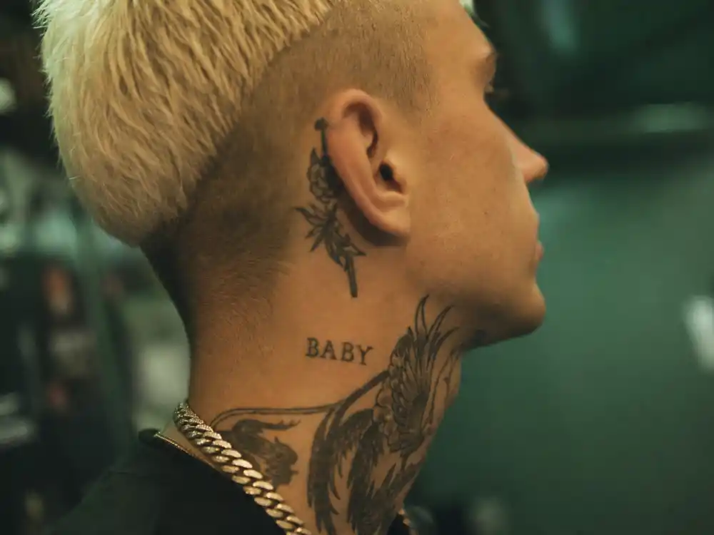 Machine Gun Kelly tattoos and their meanings neck ink — profile close-up of throat and behind-ear script tattoos