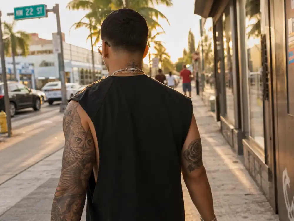 Maluma tattoos and their meanings — artist walking Miami street from behind with owl shoulder tattoo and rose on right arm at golden hour