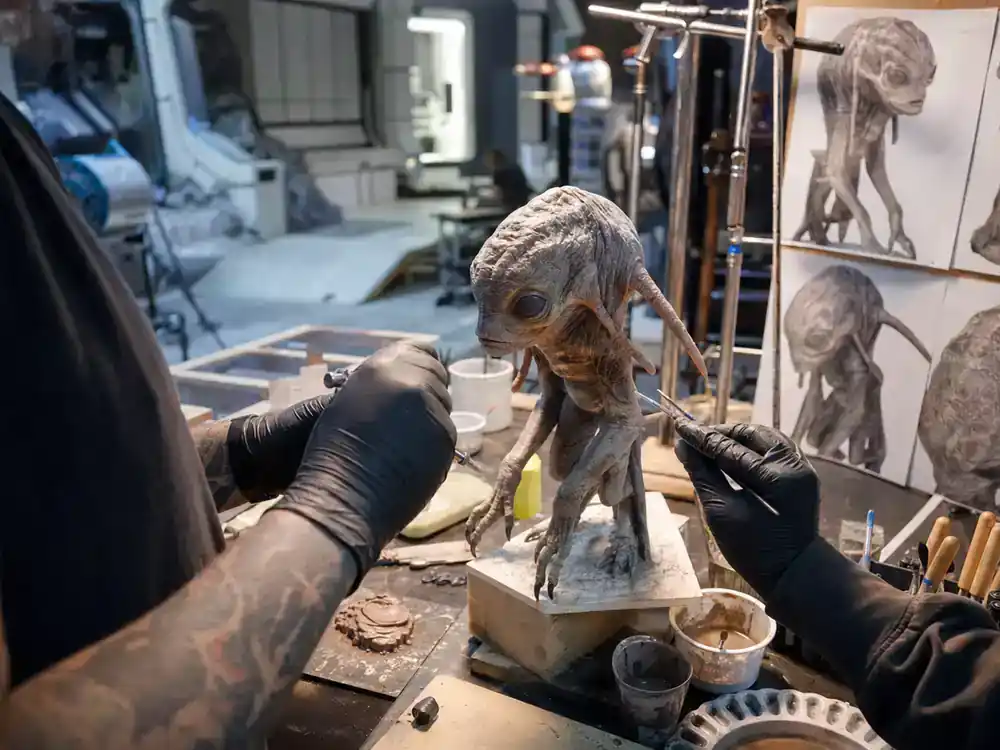 Mandalorian and Grogu movie cast explained Grogu — practical effects crew sculpting small creature prop on sci-fi film workshop bench, puppeteers visible