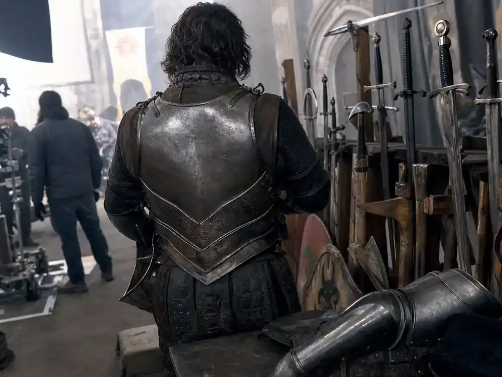 Masters of the Universe movie 2026 cast guide Idris Elba Man-At-Arms — medieval soldier armor department with weapons rack on fantasy production set from behind
