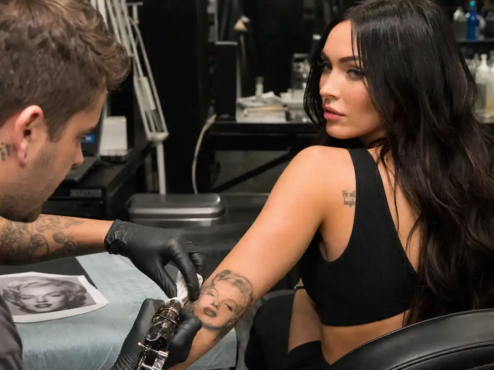 Megan Fox tattoos and their meanings — tattoo artist inking Marilyn Monroe forearm portrait during professional studio session