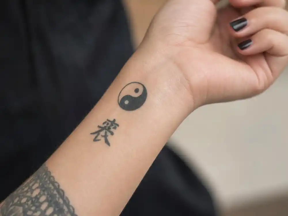 Megan Fox tattoos and their meanings — close-up of yin yang symbol and Chinese strength character on slender wrist