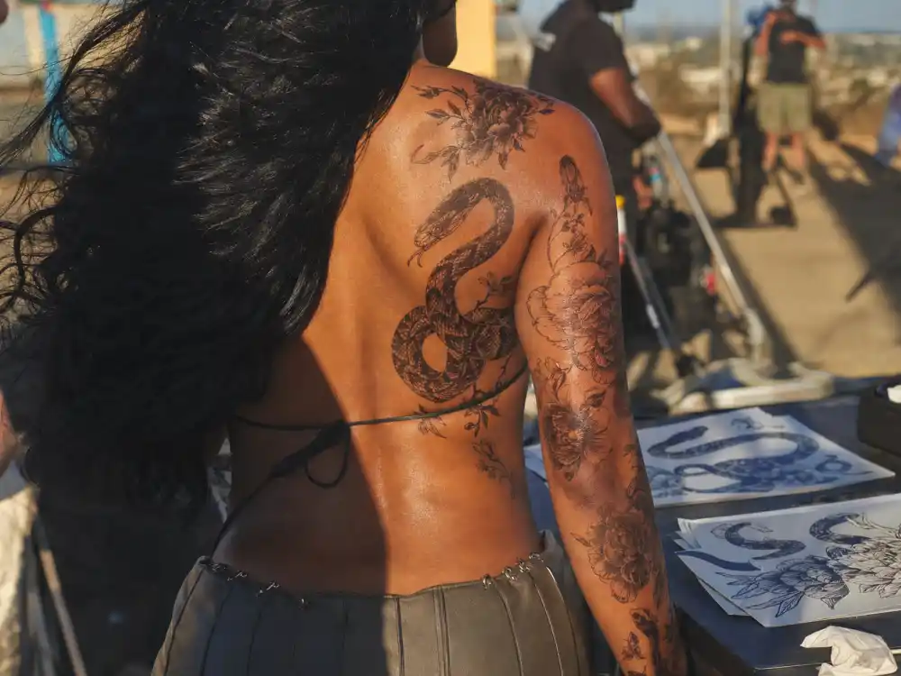Megan Thee Stallion tattoos and their meanings snake motif — temporary snake and floral Japanese body art on upper back during outdoor video shoot