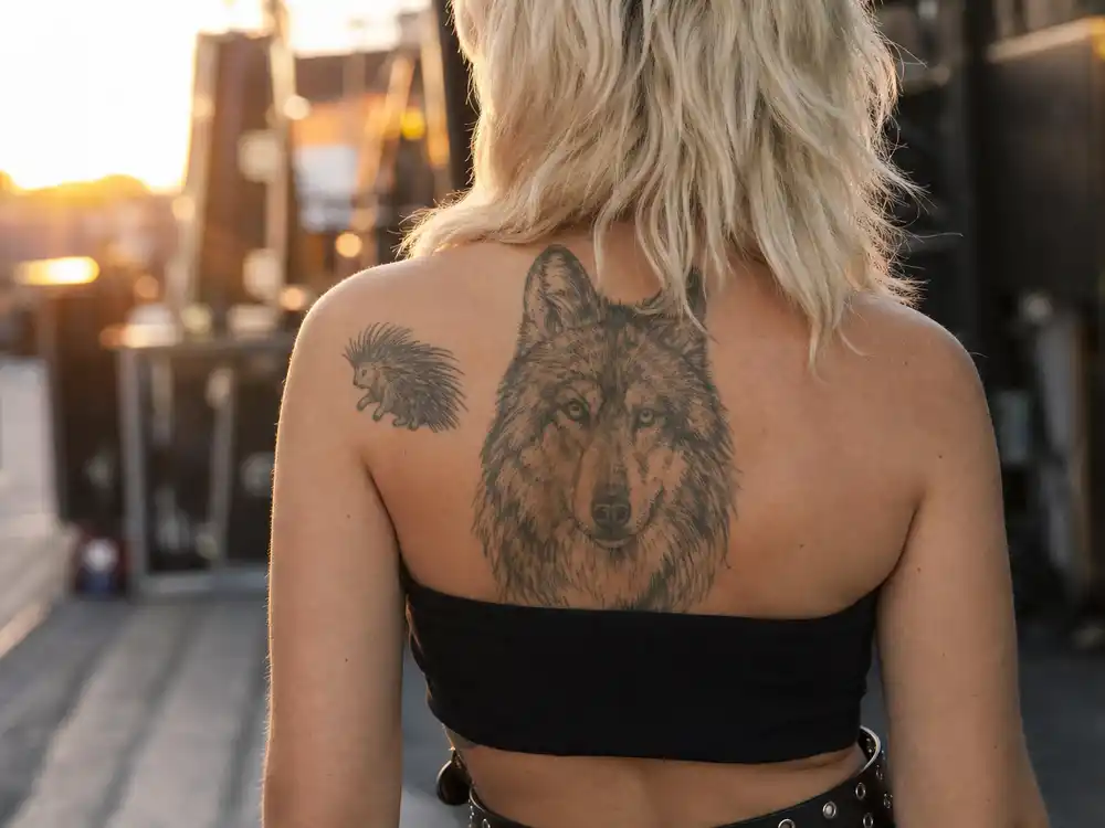 Miley Cyrus tattoos and their meanings — detailed wolf portrait shoulder tattoo and porcupine animal ink photographed from behind backstage
