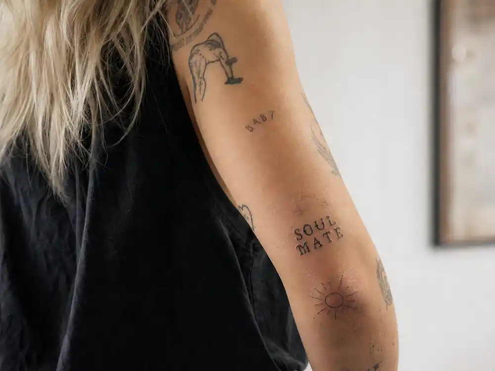 Miley Cyrus tattoos and their meanings — close-up of SOUL MATE script and sun elbow tattoo on inked forearm photographed over-shoulder