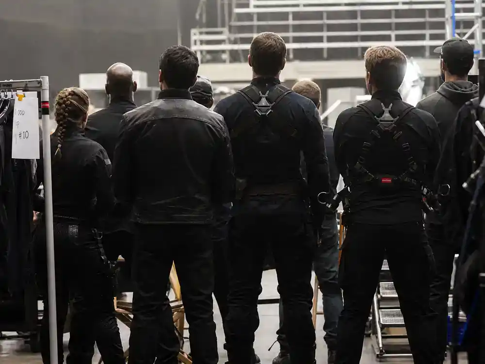 Mission Impossible 8 cast and filming facts returning ensemble — cast silhouettes from behind on action film set with stunt harnesses and costume rack