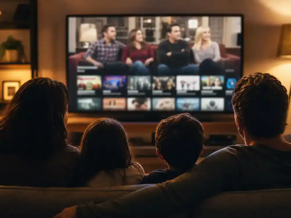 Modern Family cast net worth 2026 ranked streaming licensing — family silhouettes from behind watching sitcom comedy on living room flat screen with generic blurred interface