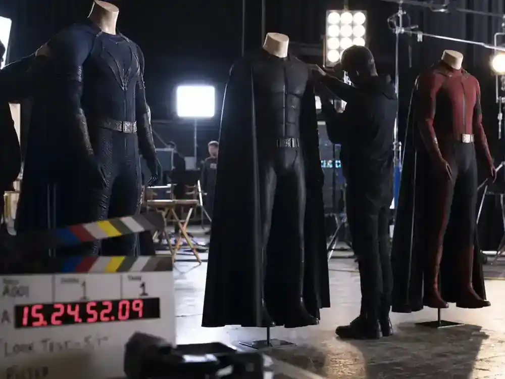 Most anticipated movies of 2026 ranked superhero blockbusters — generic hero costumes on mannequins on film soundstage with crew silhouettes, faces turned away
