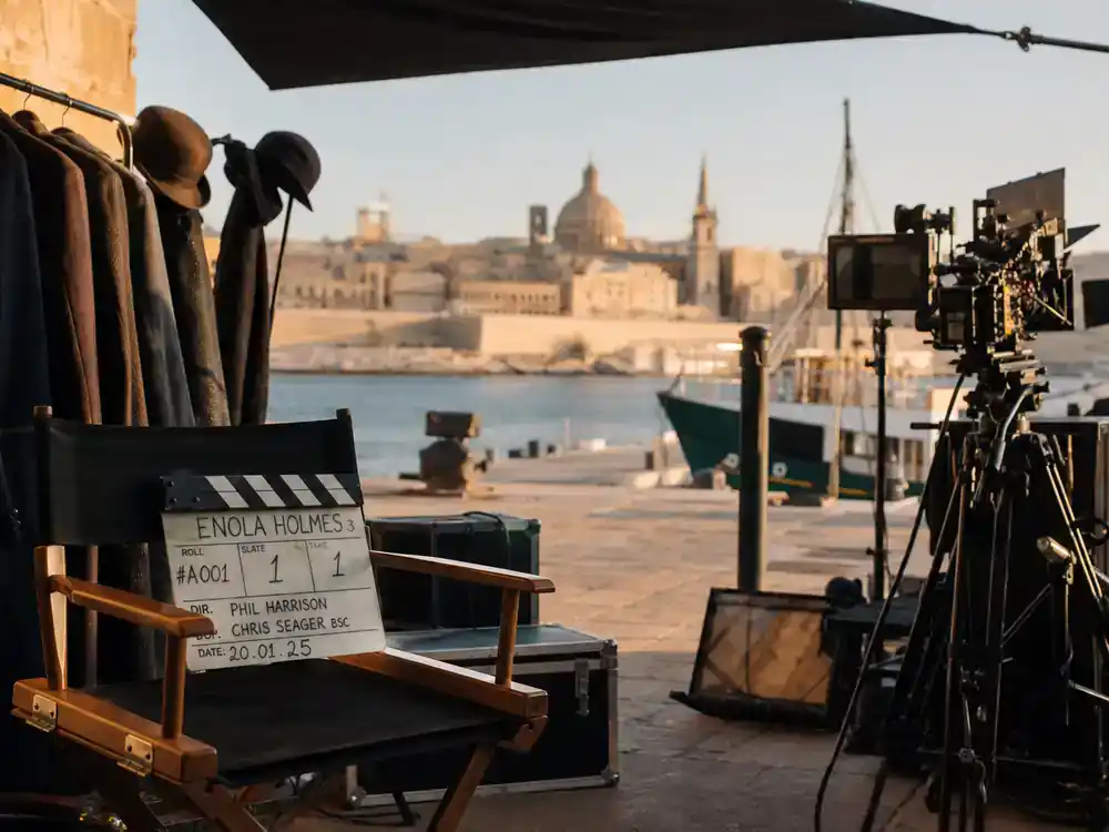 Netflix movies coming in July 2026 Enola Holmes 3 — Mediterranean film set with clapperboard and detective costume rack silhouettes, faces turned away