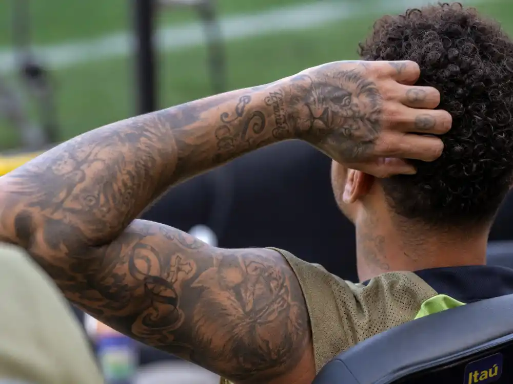 Neymar tattoos and their meanings arm sleeve — tiger lion treble clef and cross crown left arm over-shoulder angle